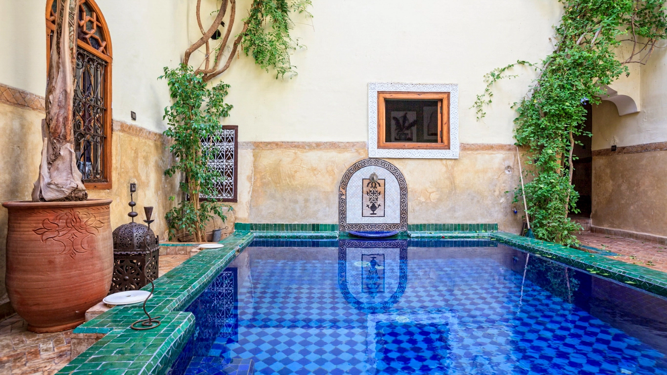Charming riad in Marrakech featuring a tranquil pool surrounded by greenery and traditional Moroccan decor, ideal for budget travelers.