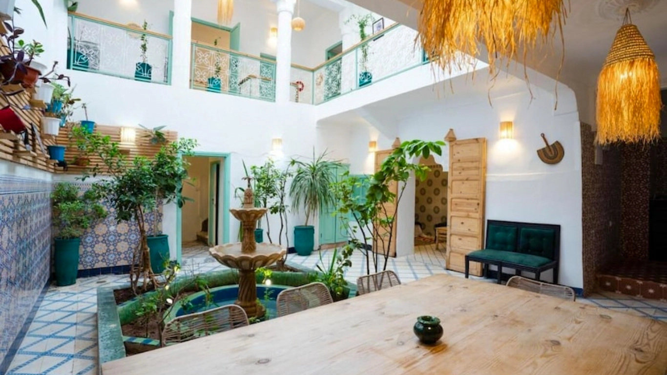 Bright courtyard of Riad Lkhlil a traditional and affordable riad in Marrakech with lush plants, a central fountain, Moroccan tilework, and cozy seating areas.
