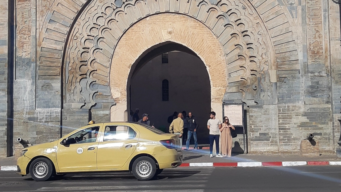 Yellow taxi in front of a historic gate in Marrakech, representing affordable public transport options for travelers exploring the city.