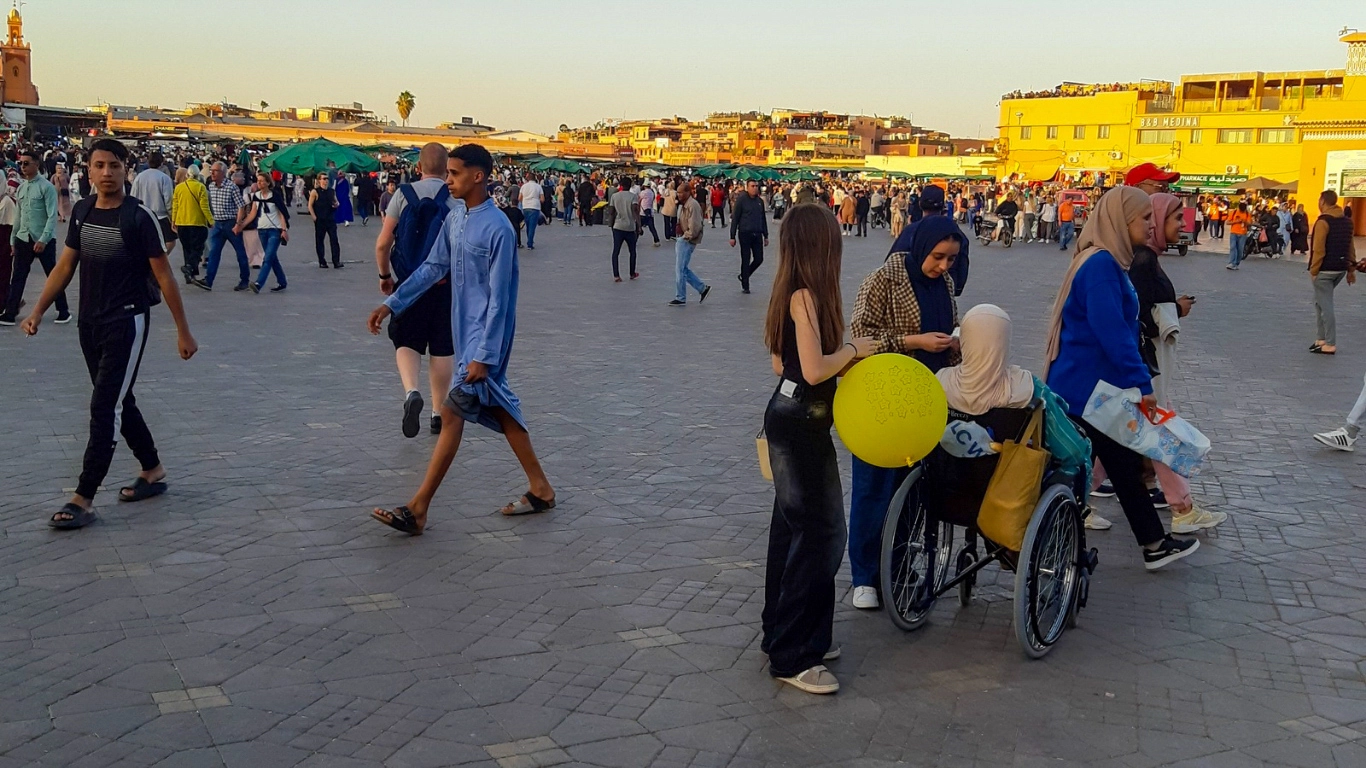 Crowds of locals and tourists in the lively main square of Jemaa el Fnaa, Marrakech, with market stalls and city buildings in the background
