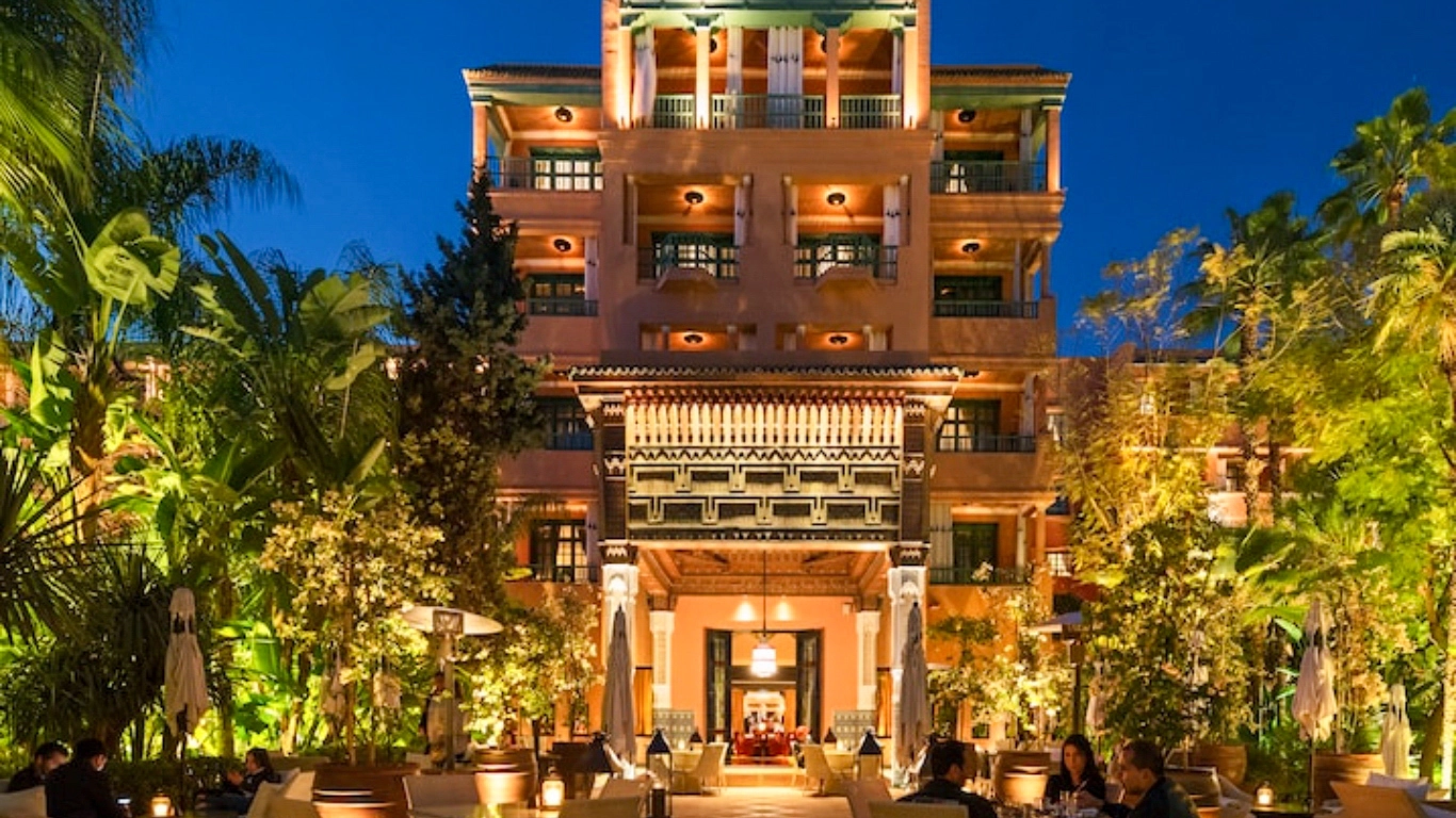 La Mamounia Marrakech luxury hotel illuminated at night with outdoor dining area and palm trees