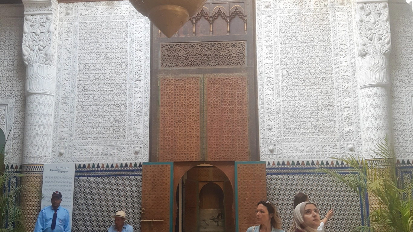 Visitors exploring the garden and courtyard of Dar El Bacha in Marrakech, featuring traditional Moroccan architecture