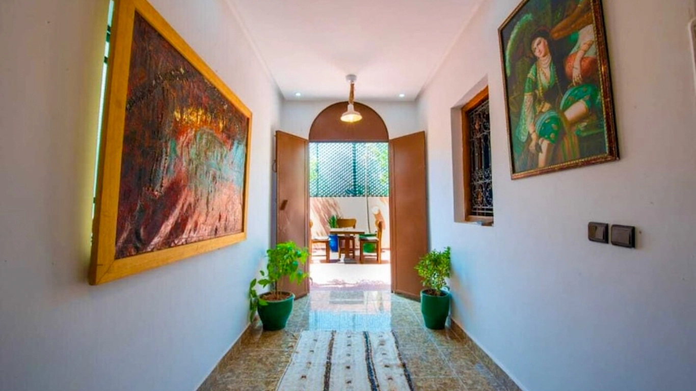 Bright courtyard of riad amely a traditional and affordable riad in Marrakech with lush plants, a central fountain, Moroccan tilework, and cozy seating areas.
