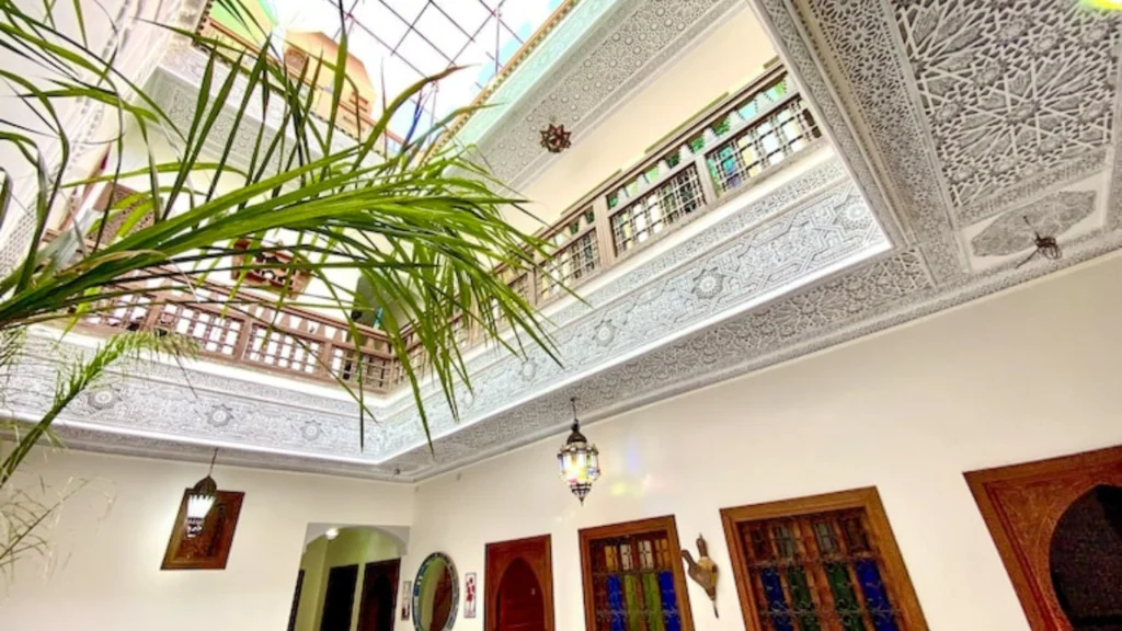 Interior view of Riad Nouhal in Marrakech showcasing intricate Moroccan architecture with decorative plasterwork and traditional lanterns.