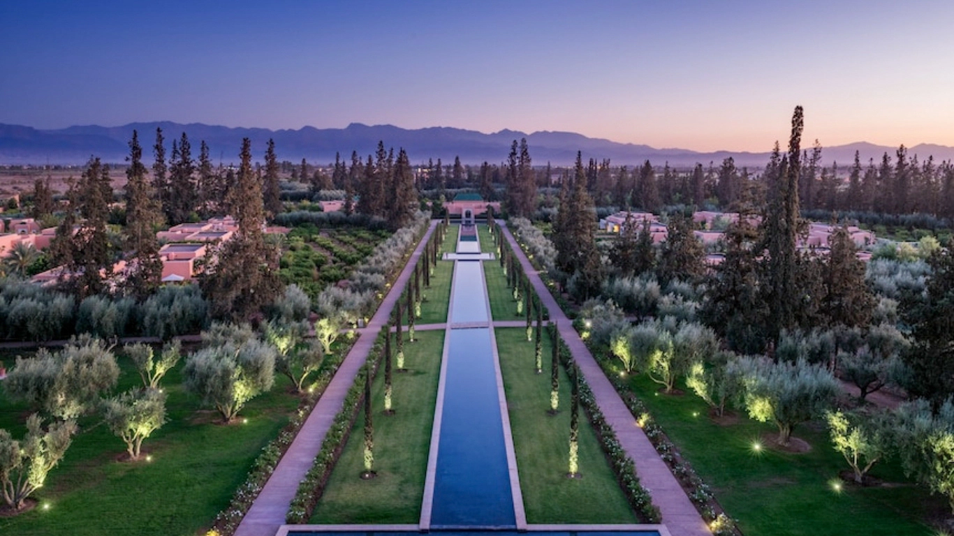 The Oberoi Marrakech luxury resort gardens with long reflecting pool and Atlas Mountains backdrop at dusk