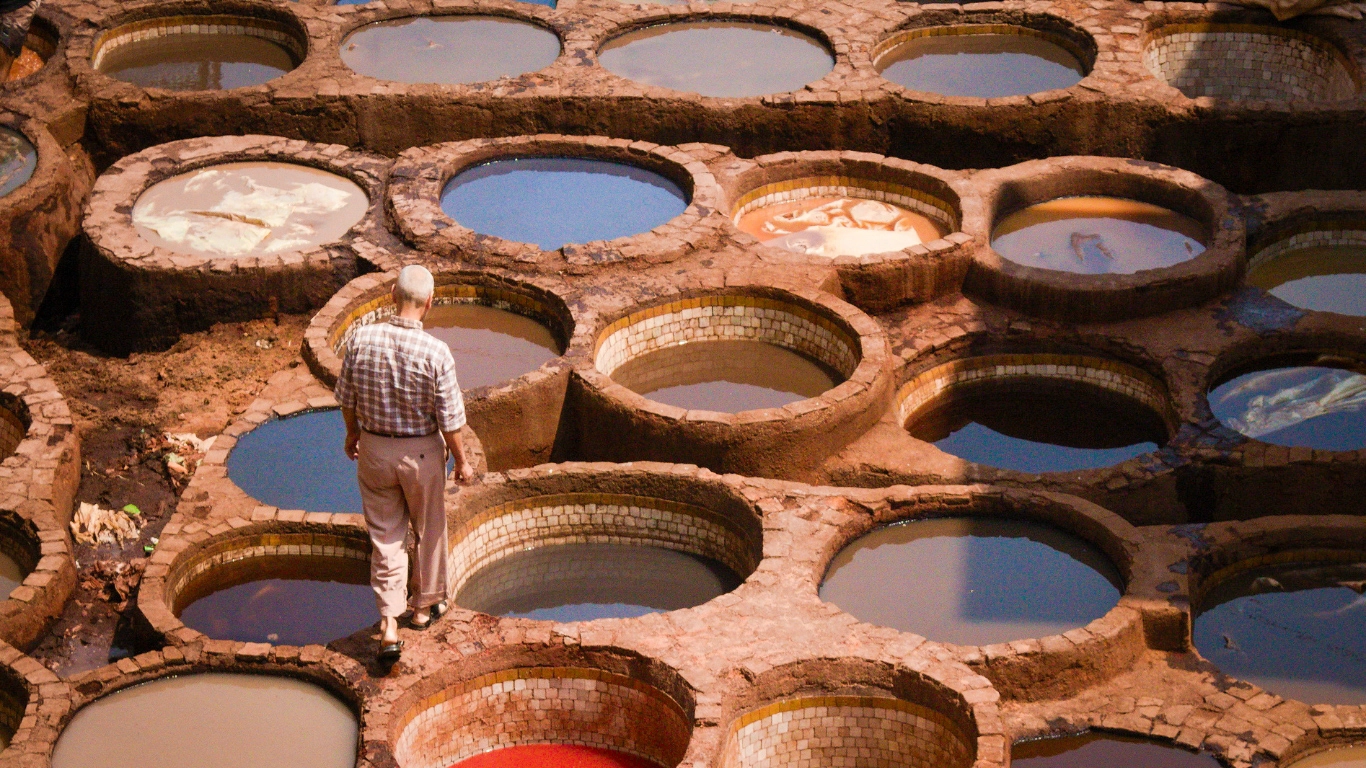A man walking through the colorful leather dyeing pits at Chouara Tannery in Fes, Morocco – a must-see stop on a 3-day trip from Marrakech to Fes.
