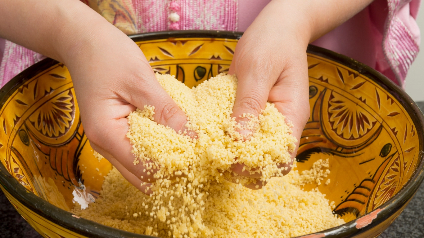 Hands handling couscous in a vibrant Moroccan bowl during a cooking workshop in Marrakech, highlighting local culinary traditions
