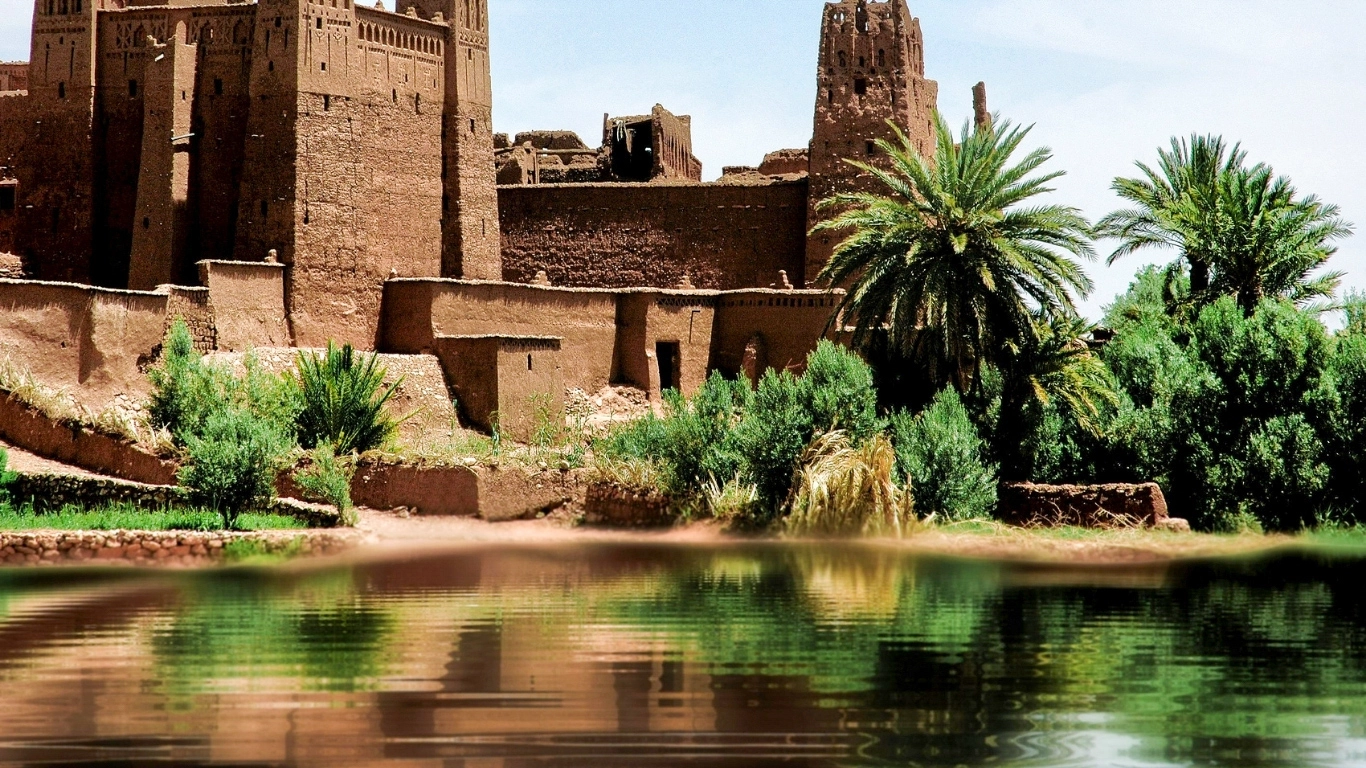 Ancient kasbah of Ait Ben Haddou with palm trees reflected in the water near Ouarzazate, Morocco
