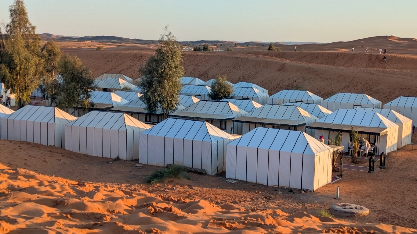 Luxury desert camp in Merzouga Sahara Morocco with white tents and sand dunes at sunset
