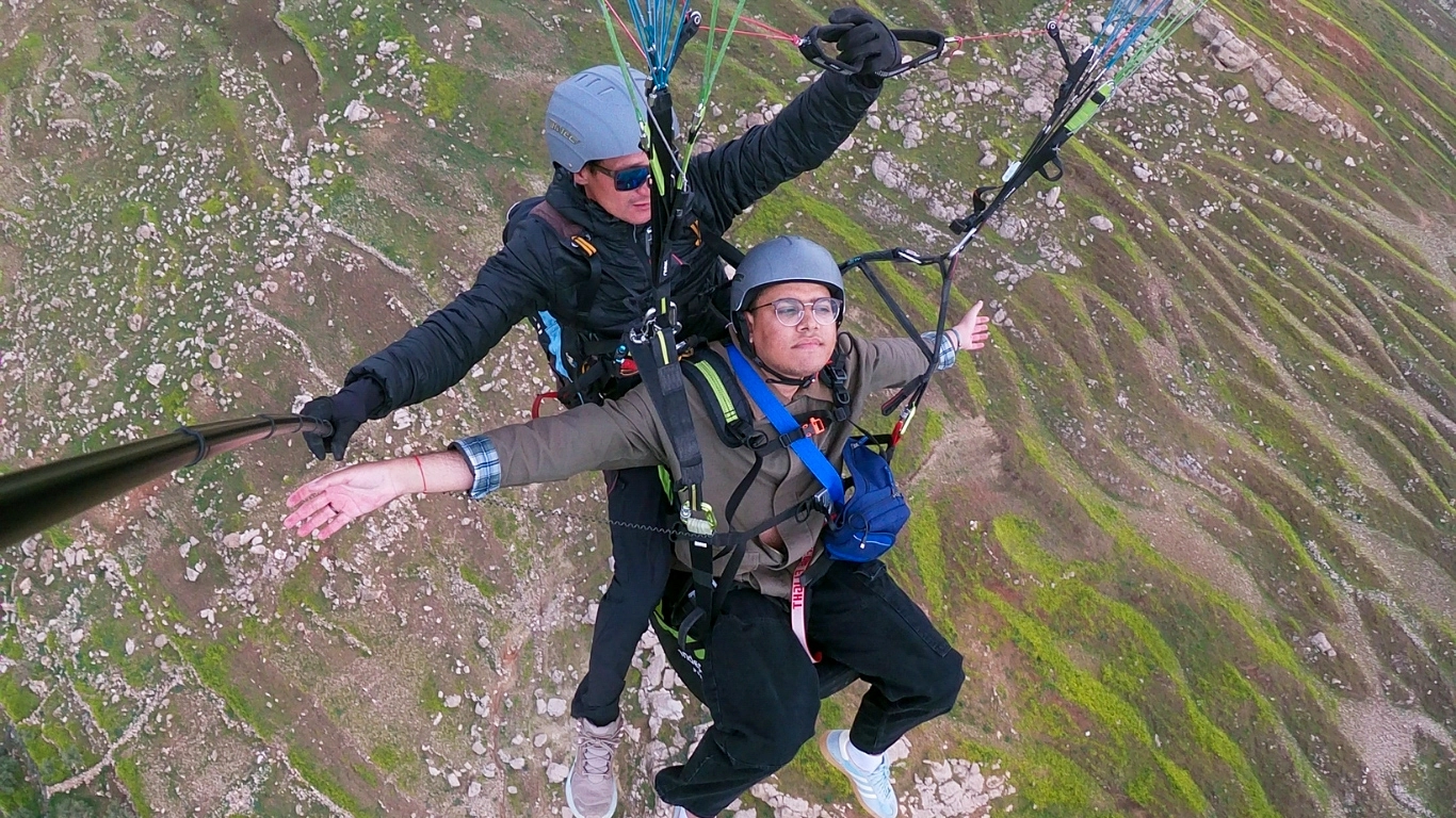 Tandem paragliding over Kik Plateau near Marrakech, Morocco, with Atlas Mountains landscape below.