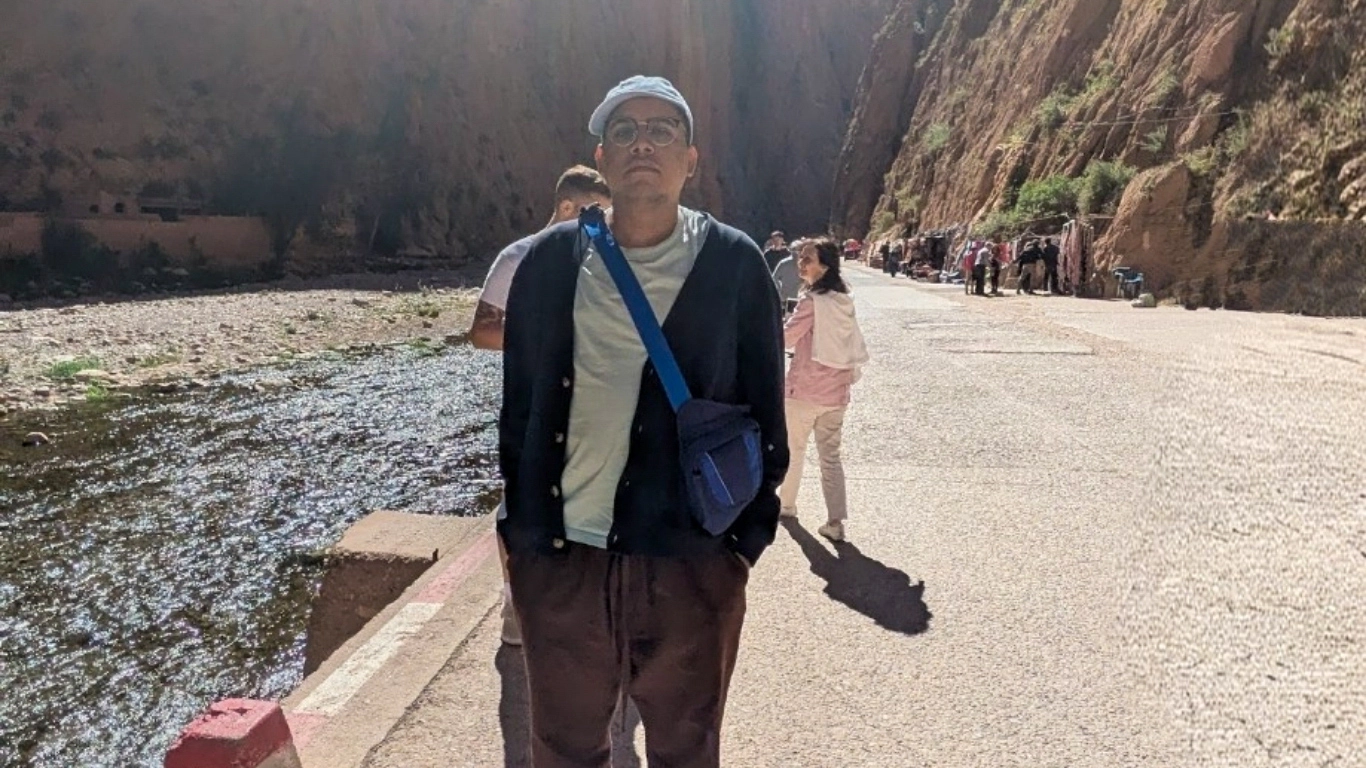 Traveler standing in Todgha Gorges in Morocco, with towering red canyon walls and visitors walking along the gorge road.
