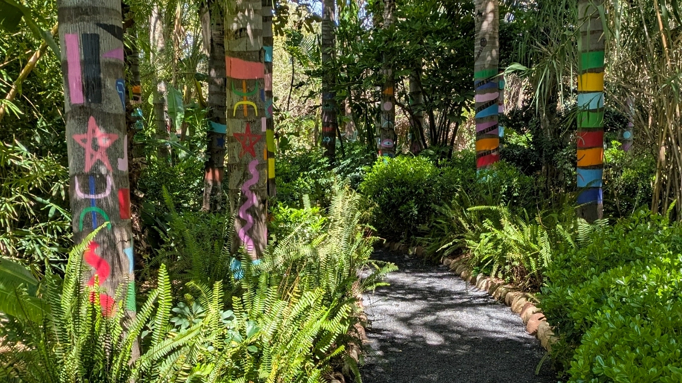 Lush garden pathway with colorful hand-painted tree trunks and tropical ferns at Anima Garden Marrakech