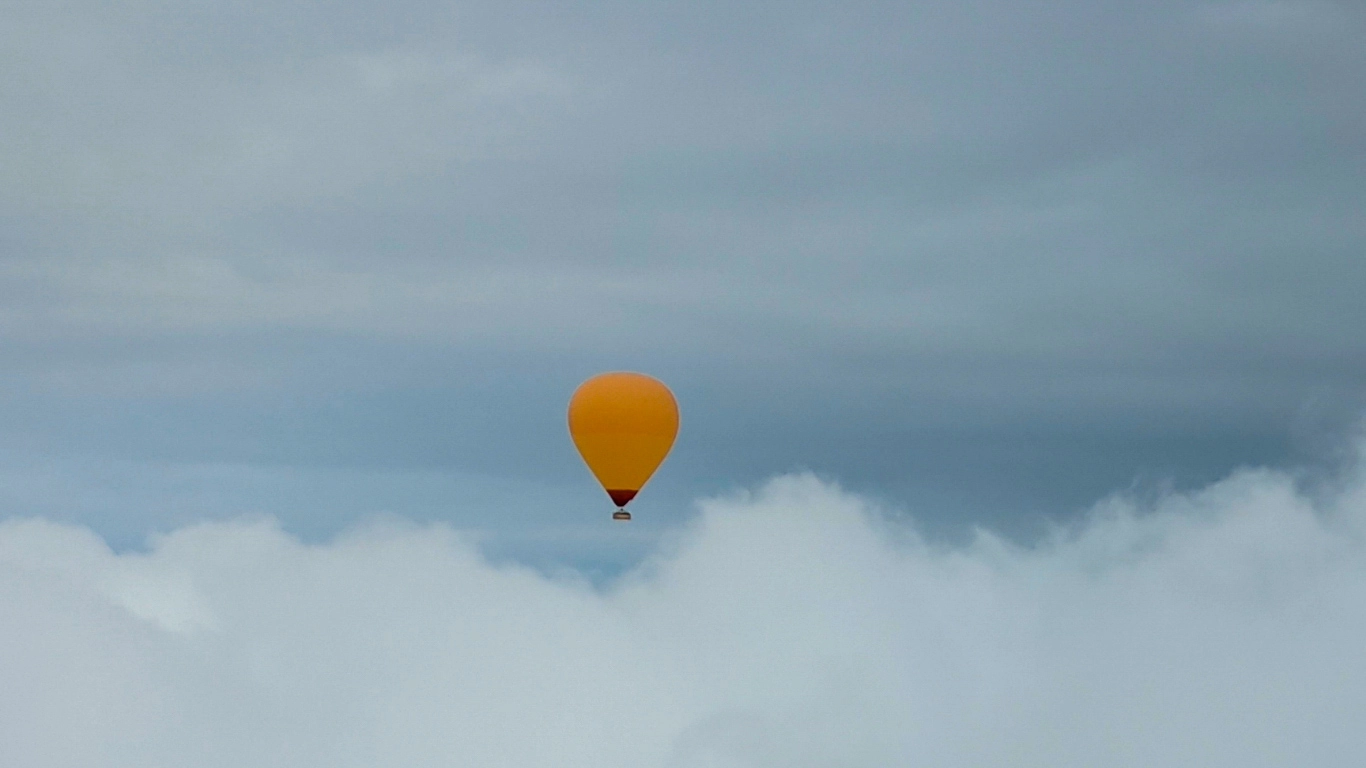 Orange hot air balloon flying above the clouds near Marrakech, Morocco, during an early morning Atlas Mountains balloon flight.